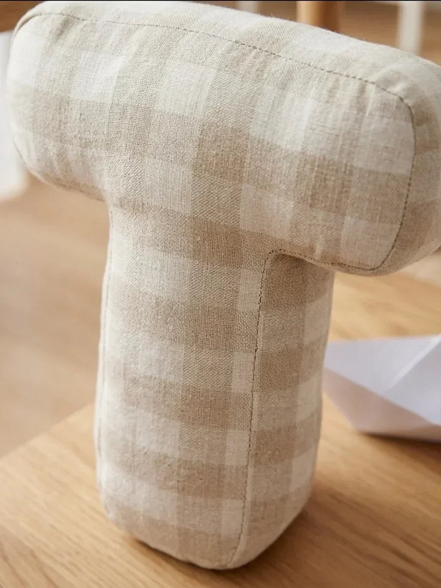 Decorative beige plaid cushion in the shape of the letter T on a wooden table in a nursery.