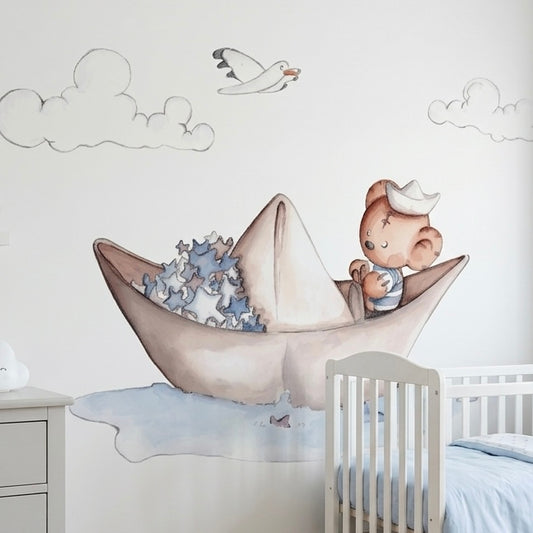 Vinilo decorativo infantil que muestra un oso marinero en un barquito de papel, rodeado de nubes y una gaviota.