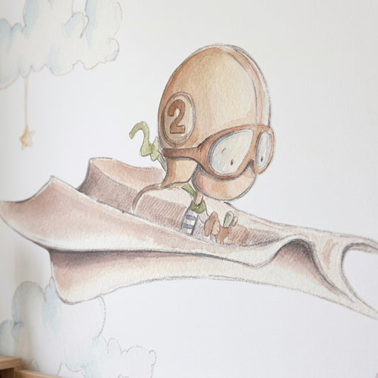 Vinilo decorativo infantil que muestra un pequeño aviador volando en un avión de papel entre nubes suaves y esponjosas.