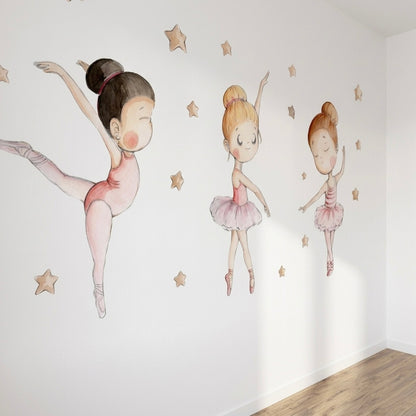 Three charming ballet dancers are illustrated on a white wall, each in different poses, wearing pink tutus and ballet shoes. Golden stars are scattered around them, creating a whimsical and enchanting atmosphere, perfect for a childs room.