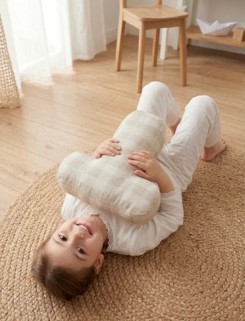 Smiling child in white pajamas lying on round woven rug, holding a soft cushion in cozy nursery