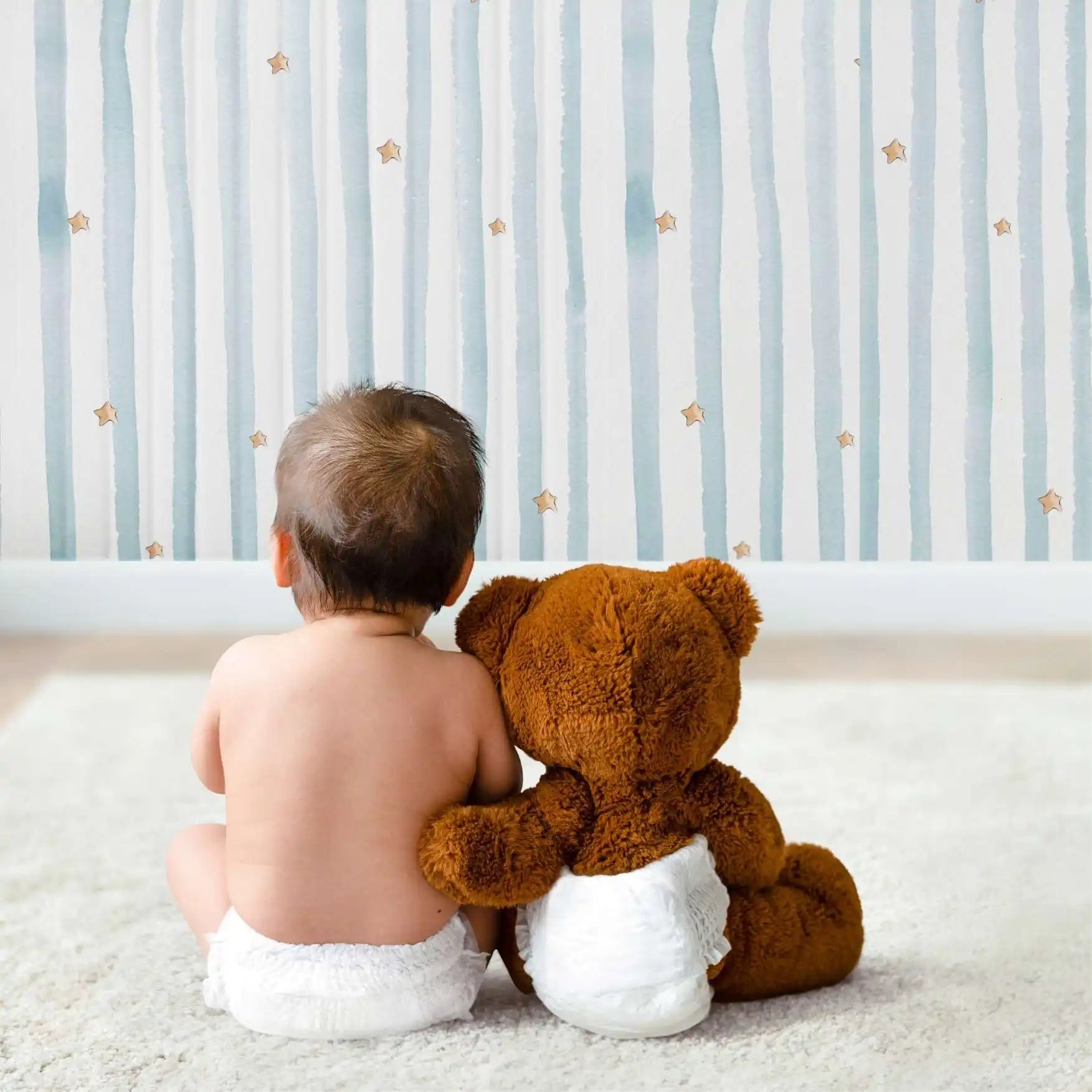 Un bebé en un pañal sentado al lado de un oso de peluche marrón.